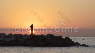 渔夫的剪影，日落时在岩石上钓鱼的人。 120fps